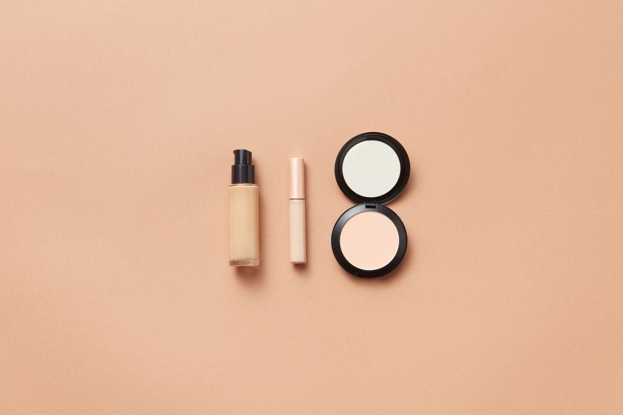 Flatlay of foundation, concealer, and compact powder on beige background. Perfect for beauty and cosmetic themes.